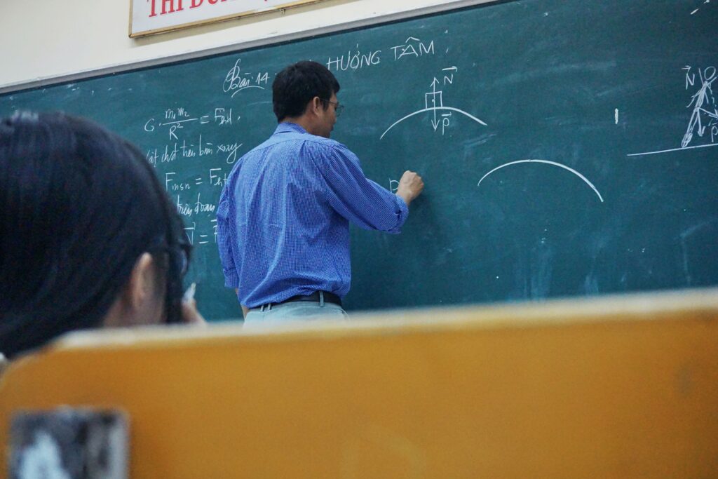 A professor has his back to the class as he writes on a chalkboard.
